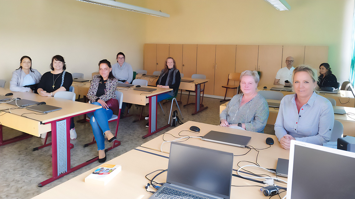 Neun Erwachsene Menschen sitzen in einem Computerraum in ihrer ehemaligen Schule.