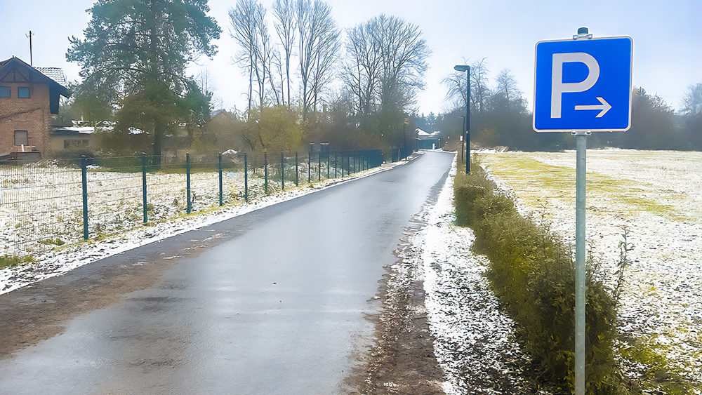 Eine Zufahrtsstraße zu einem Wohngebiet mit einem Parkplatzschild und Bäumen.