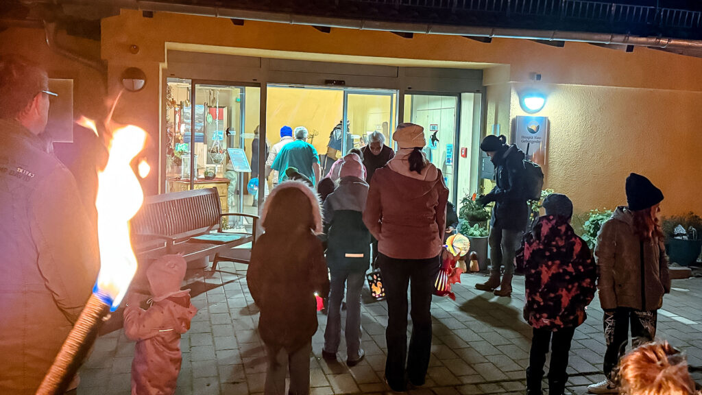 Kinder mit Fackeln, Lampions und Lichter vor dem hell erleuchteten Eingang zu einem Altenheim.