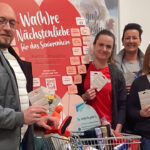 **ALT-Text:** Vier Personen posieren vor einem Plakat mit der Aufschrift "Wa(h)re Nächstenliebe für das Seniorenheim". Sie halten Wunschzettel in den Händen und stehen neben einem Einkaufswagen voller Spenden. Das Bild zeigt die erfolgreiche Teilnahme an einer ROSSMANN-Spendenkampagne für das Haus Harztor.
