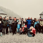 Gruppe von etwa 26 Wanderinnen und Wanderern, darunter Kinder und Erwachsene, posiert lachend vor der Nordhäuser Talsperre bei nebligem Wetter.