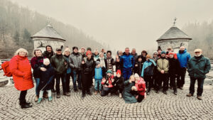 Gruppe von etwa 26 Wanderinnen und Wanderern, darunter Kinder und Erwachsene, posiert lachend vor der Nordhäuser Talsperre bei nebligem Wetter.