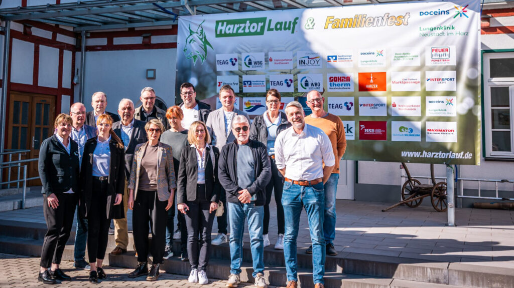 Gruppenfoto der Organisatoren und Sponsoren des Harztorlaufs 2025 vor dem Banner mit den Logos der Partner am Mehrzweck-Gebäude in Harztor.