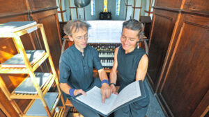 Das Duo Vimaris bei der Vorbereitung auf das Konzert an der Ladegast-Orgel in der St.-Georg-Kirche Neustadt/Harz: Dr. Wieland Meinhold zeigt auf eine Notenstelle, während Mirjam Meinhold mit einem Lächeln zuhört. Im Hintergrund die historische Orgel und der Blick ins Kirchenschiff mit bunten Glasfenstern.