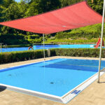 Neues Planschbecken im Waldbad Ilfeld mit rotem Sonnensegel, im Hintergrund das große Schwimmbecken in grüner Waldlandschaft