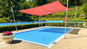 Neues Planschbecken im Waldbad Ilfeld mit rotem Sonnensegel, im Hintergrund das große Schwimmbecken in grüner Waldlandschaft