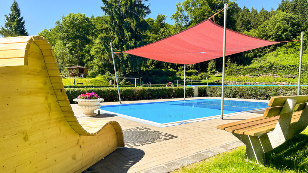 Holzliege, Bank und überdachtes Planschbecken im Waldbad Ilfeld an einem sonnigen Sommertag