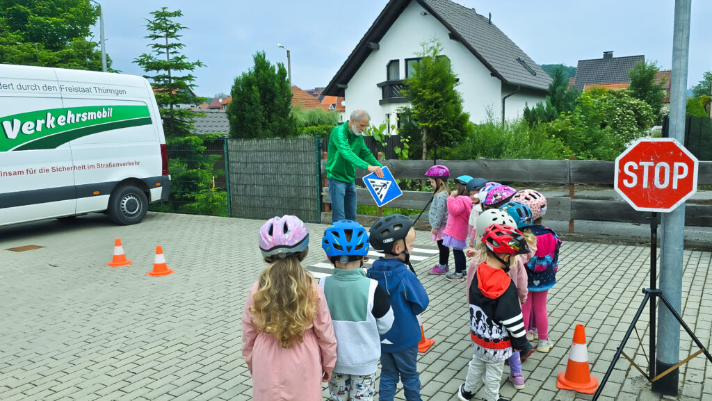 Kinder mit Helmen lauschen Trainer, der ein Zebrastreifen-Verkehrsschild zeigt.