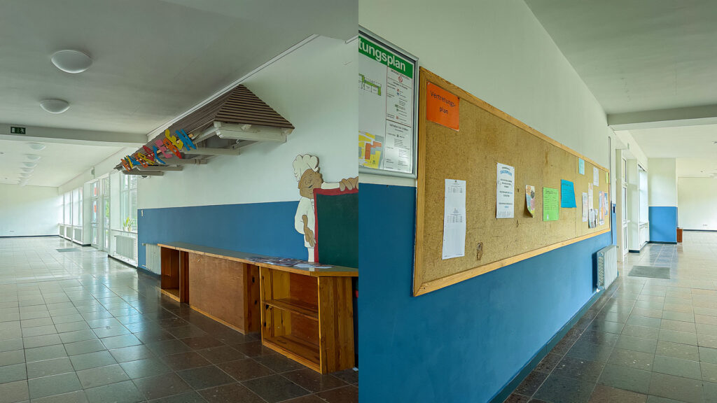 Heller Schulflur mit blauem Sockel und weißen Wänden; links Holztheke/Deko, rechts lange Pinnwand mit Aushängen, viel Tageslicht durch Fensterfront.