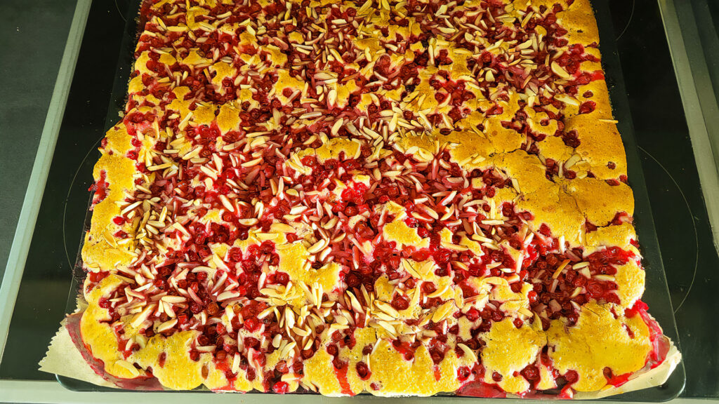 Frisch gebackener Johannisbeer-Blechkuchen mit gestifteten Mandeln auf einem Backblech – goldbraun und saftig.