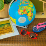 Thematisch dekorierte Ecke mit Reisezubehör: Weltkugel, Sonnenbrille, Flip-Flops und einem Bild von einem Strandstuhl – Urlaubsstimmung im Aufenthaltsraum.