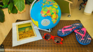Thematisch dekorierte Ecke mit Reisezubehör: Weltkugel, Sonnenbrille, Flip-Flops und einem Bild von einem Strandstuhl – Urlaubsstimmung im Aufenthaltsraum.