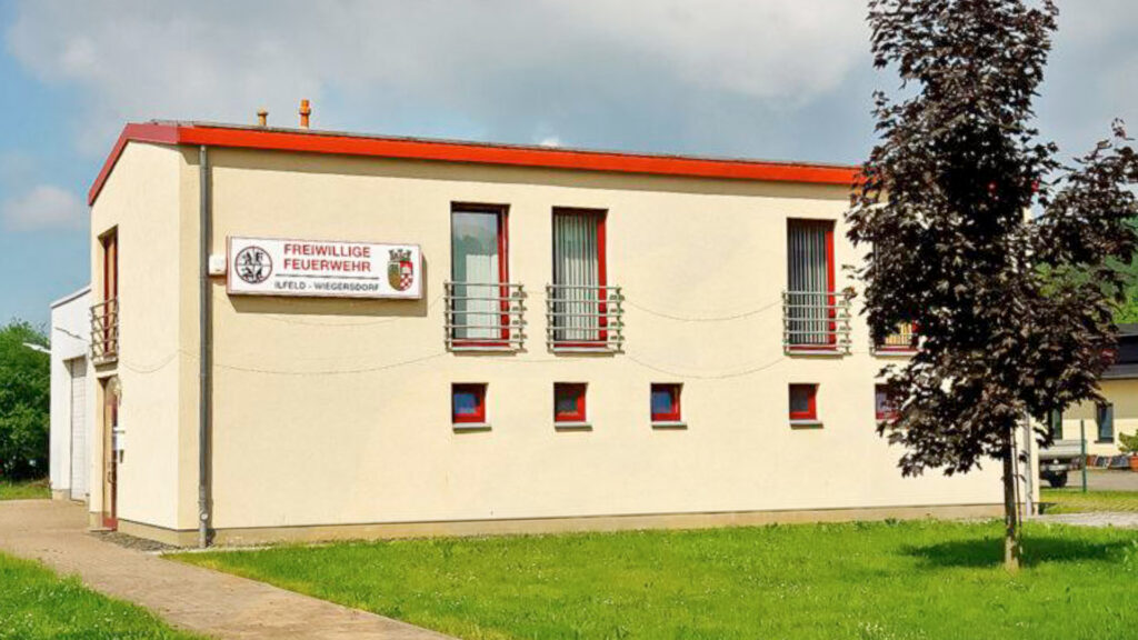 	2.	Modernes Feuerwehrgerätehaus der Freiwilligen Feuerwehr Ilfeld-Wiegersdorf: zweigeschossiger, heller Bau mit roten Fensterrahmen und Beschilderung, davor Rasenfläche und junger Baum.