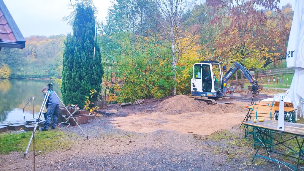 Zwei Schüler verlegen Pflastersteine auf der Bühne am Gondelteich. Ein Handwerker erklärt die Arbeitsschritte, Werkzeuge liegen griffbereit auf dem Boden.