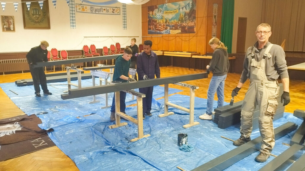 Elektriker der Firma Hahn montieren Leitungen und Steckdosen am Kioskbereich. Kabelrollen, Werkzeug und Sicherheitswesten prägen das Bild.