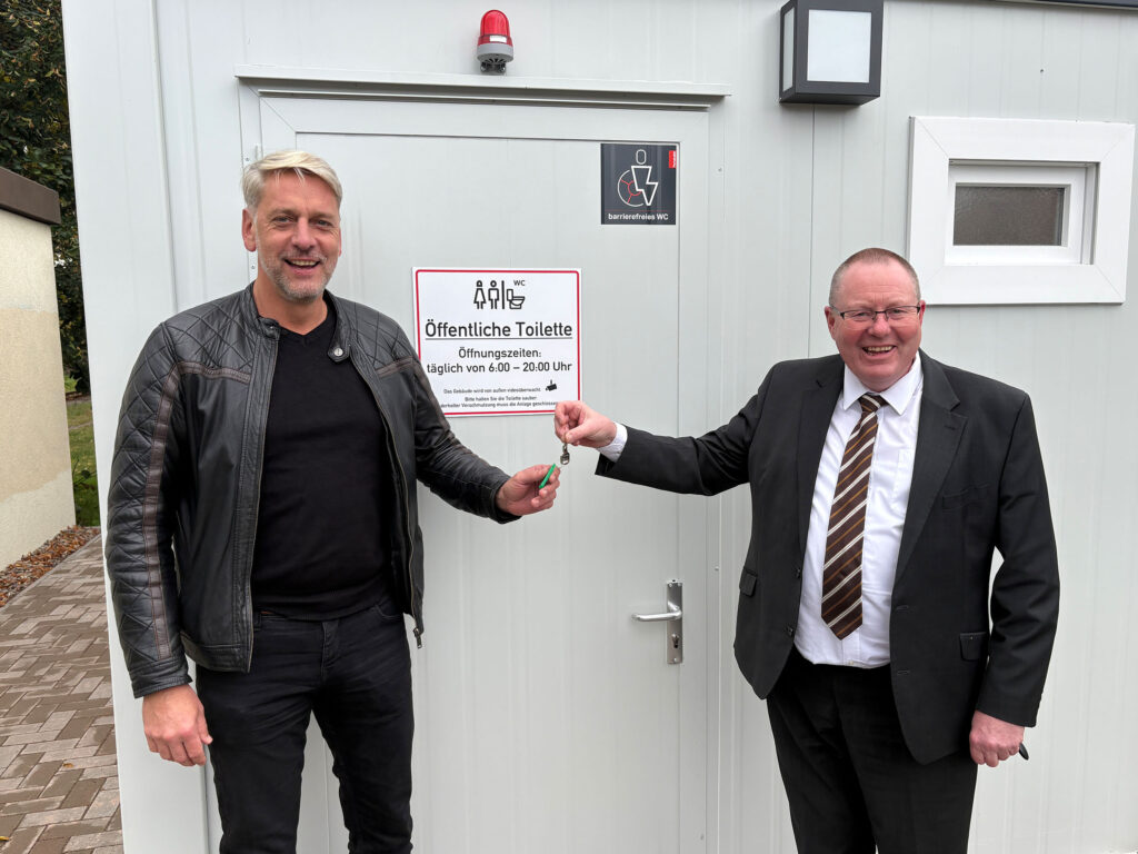 Thorsten Schwarz, Geschäftsführer der Verkehrsbetriebe Nordhausen, und Harztors Bürgermeister Stephan Klante übergeben symbolisch den Schlüssel zur neuen öffentlichen Toilette am Bahnhof Niedersachswerfen Ost.