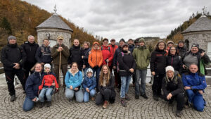 Gruppenfoto der Harztor-Wandergruppe auf dem Staudamm der Nordhäuser Talsperre; rund 30 Personen zwischen zwei kleinen Steintürmen, herbstlicher Wald im Hintergrund, bedeckter Himmel.