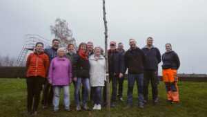 Zehn Mitglieder des Arreé-Traditionsvereins und des Ortschaftsrates pflanzen gemeinsam einen jungen Lederhülsenbaum auf der grünen Liegewiese des Freibads Niedersachswerfen. Im Hintergrund sind die leeren Edelstahlbecken des Bades zu sehen.