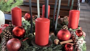 Ein weihnachtliches Gesteck mit Tannenzweigen und roten Kerzen.