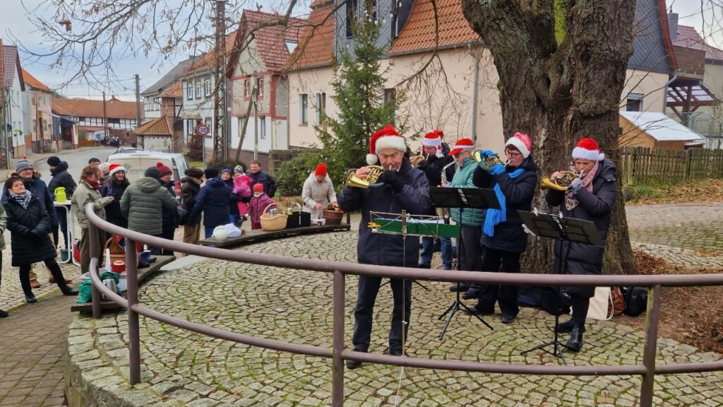 Die Bläsergruppe Neustadt-Osterode steht neben einem großen Baum, mehrere Passanten hören zu.