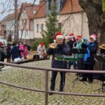 Die Bläsergruppe Neustadt-Osterode steht neben einem großen Baum, mehrere Passanten hören zu.
