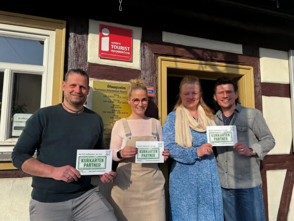 Vier Personen stehen lächelnd vor dem Eingang der Tourismus-Information Neustadt und halten jeweils ein grünes Schild mit der Aufschrift „Kurkarten-Partner" in die Kamera. Von links: Roland Gerlach, Alexandra Günther, Ariane Bruchmann und Sascha Niedenführ.