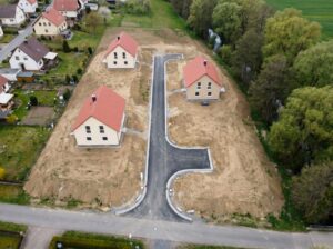 Symbolfoto vom Baugebiet Eberthof in Niedersachswerfen. Auf einer leicht geneigten Fl&auml;che stehen drei fertige Einfamilienh&auml;user mit roten Satteld&auml;chern, dazwischen liegen noch unbebaute Grundst&uuml;cke. Eine frisch asphaltierte Erschlie&szlig;ungsstra&szlig;e mit Wendeanlage f&uuml;hrt durch das Gebiet. Im Osten begrenzt ein Streifen aus hohen Erlen und Weiden den Uferbereich der Bere, im Westen schlie&szlig;t &auml;ltere Wohnbebauung an. KI.