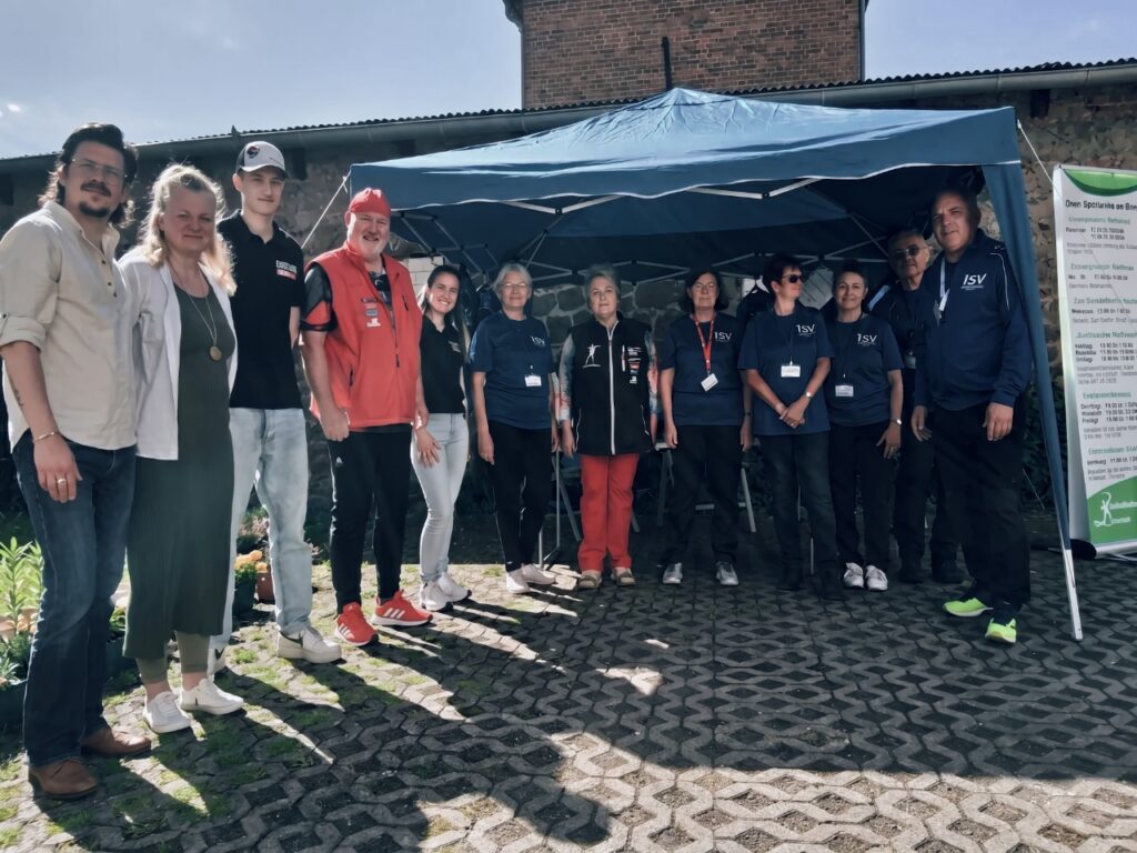 Das Team des RSV-Ilfeld in blauen Vereinsshirts steht mit Gästen unter einem blauen Pavillon. Rechts ist ein grünes Banner mit Vereinsinformationen zu sehen.