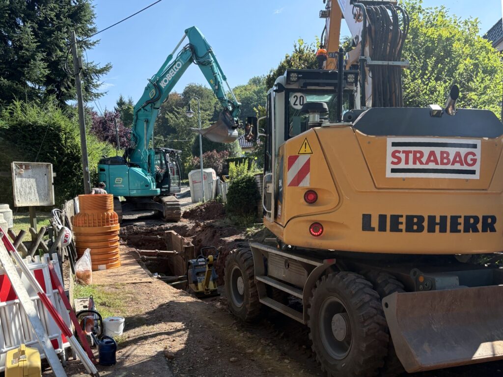Baustelle in der Neuen Marktstraße in Ilfeld. Zwei Bagger stehen am offenen Graben, davor liegen orangefarbene Schachtringe. Rot-weiße Absperrungen sichern die Baustelle.
