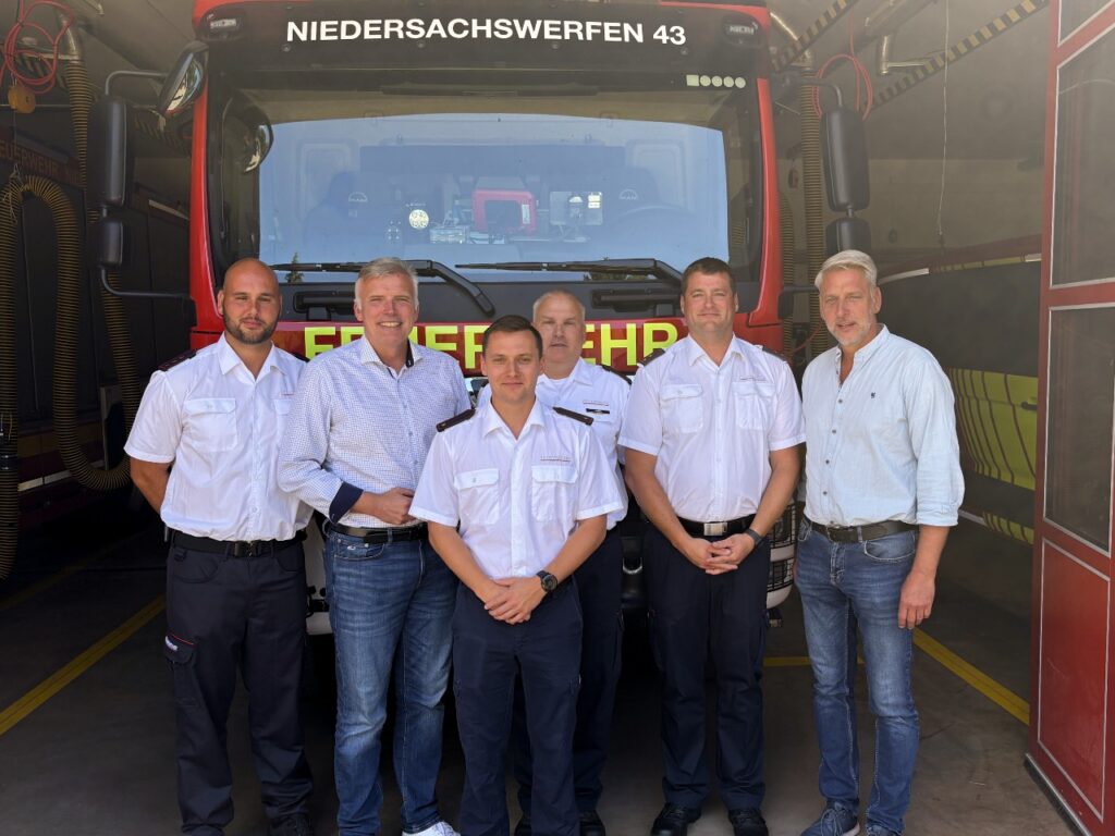 Sechs Männer stehen vor einem roten Löschfahrzeug mit der Aufschrift "Niedersachswerfen 43" in der Fahrzeughalle. Vier von ihnen tragen weiße Diensthemden der Feuerwehr und dunkle Hosen. Dazwischen stehen Staatssekretär Andreas Bausewein im weiß karierten Hemd und rechts außen Bürgermeister Stephan Klante im hellen Hemd. Alle schauen in die Kamera.