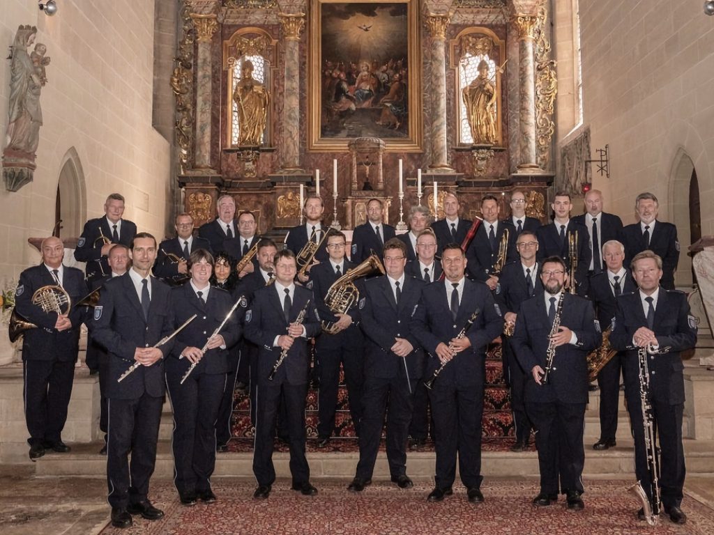 Gruppenfoto des Polizeiorchesters Thüringen in dunkelblauer Uniform mit Blasinstrumenten vor dem goldenen Barockaltar der St. Georg-Marien-Kirche in Ilfeld.