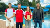 Gruppenfoto am Beckenrand des Waldbades: Shayenne Kara mit Geschenk in der Mitte, links flankiert von Schwimmmeister Roland Gerlach und seinem Kollegen Steven Klante sowie rechts Bürgermeister Stephan Klante – im Hintergrund die blaue Rutsche des Freibades Niedersachswerfen.