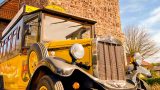 Historischer gelber Oldtimer-Bus mit schwarzem Dach und großen Rundscheinwerfern, aufgenommen vor einer alten Natursteinmauer bei Sonnenschein.