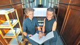 Das Duo Vimaris bei der Vorbereitung auf das Konzert an der Ladegast-Orgel in der St.-Georg-Kirche Neustadt/Harz: Dr. Wieland Meinhold zeigt auf eine Notenstelle, während Mirjam Meinhold mit einem Lächeln zuhört. Im Hintergrund die historische Orgel und der Blick ins Kirchenschiff mit bunten Glasfenstern.