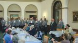 Ein Männerchor in grauen Sakkos singt in der Aula der Neanderklinik Harzwald vor zahlreichen Seniorinnen und Senioren. Die Zuhörer sitzen an festlich gedeckten Tischen, während die Sänger in Reihen stehen und aus Notenmappen vortragen. Die Stimmung wirkt konzentriert und herzlich.