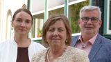 Pressefoto beim 19. Thüringer Pflegesymposium in Ilfeld-Harztor: drei Personen im Halbportrait vor grünen Fensterrahmen – mittig Frau mit Perlenkette, links Frau in weißer Jacke, rechts Mann mit Brille.