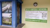 An einer hellgrünen Hauswand hängt ein großes grün-weißes Schild mit der Aufschrift „Jetzt Vorteile sichern: mit der Kurkarte für Tagesgäste!". Rechts auf dem Schild ist ein QR-Code zu sehen, unten die Adresse www.harztor-erlebenswert.de. Links daneben ein blau gerahmtes Fenster mit Landschaftsbildern aus dem Südharz.