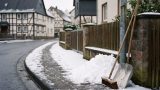 Geräumter Gehweg vor Wohngrundstücken nach leichtem Schneefall; Schnee liegt seitlich, die Fahrbahn bleibt frei. KI.
