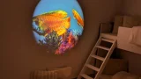 Abgedunkelter Ruheraum (Snoezelraum) mit Hochbett und Kissen; runde Wandprojektion zeigt bunte Fische über Korallen – beruhigende Unterwasserstimmung.